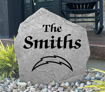 Custom Los Angeles Chargers Name Stone displayed in a landscaped flower bed, showcasing personalized family lettering and officially licensed team artwork. This decorative outdoor stone creates a striking focal point for Chargers fans and outdoor living spaces.