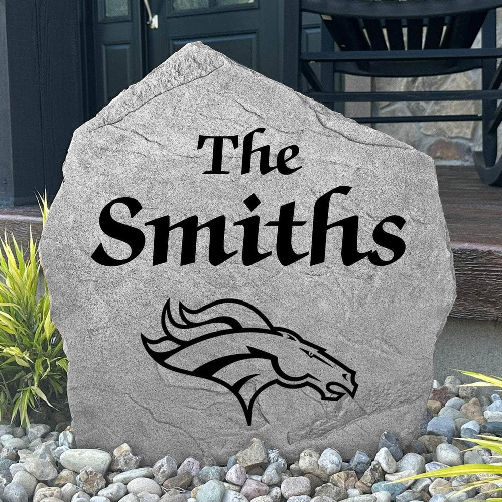 Custom Denver Broncos Name Stone displayed in a landscaped flower bed, showcasing personalized family lettering and officially licensed team artwork. This decorative outdoor stone creates a striking focal point for Broncos fans and outdoor living spaces.