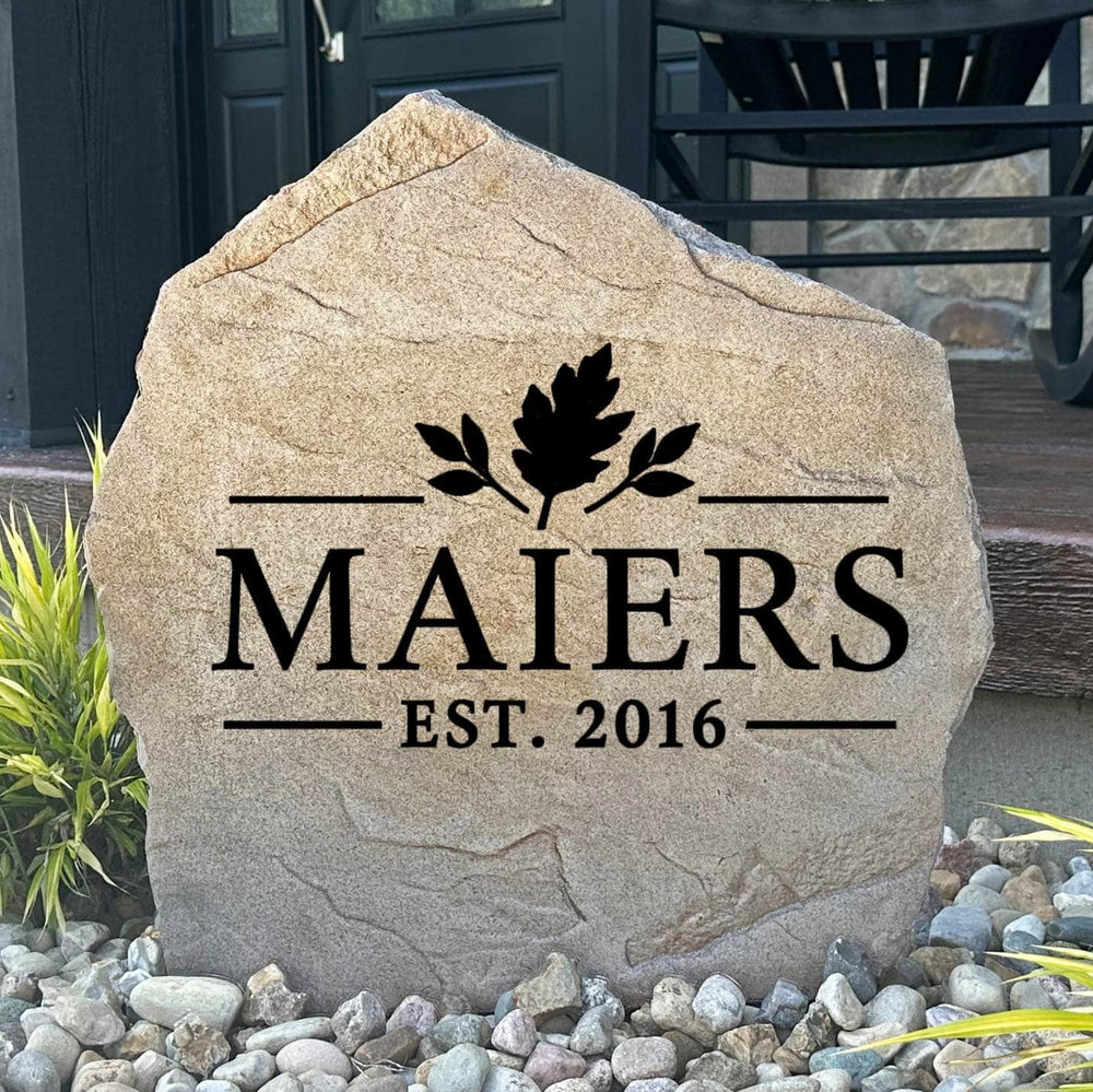 Fall Name Stone engraved MAIERS Est. 2016 with an oak leaf design, set in river rock beside a front porch