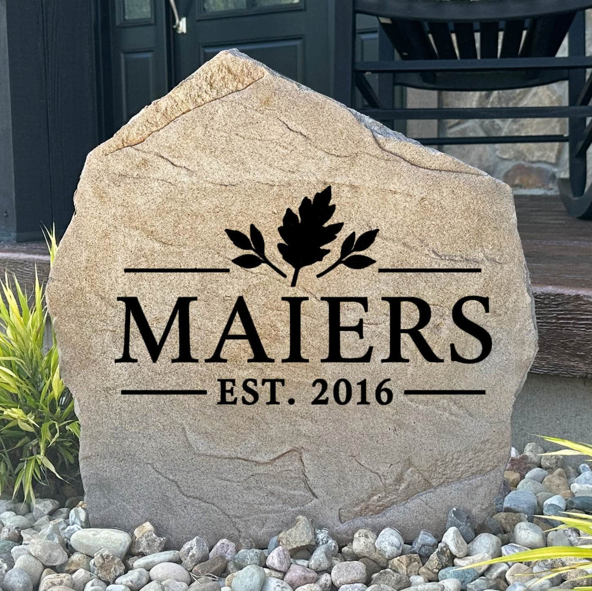 Fall Name Stone engraved MAIERS Est. 2016 with an oak leaf design, set in river rock beside a front porch
