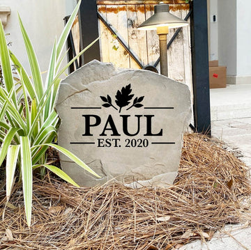 Personalized Fall Name Stone reading PAUL Est. 2020 on pine straw beside a rustic garden gate and landscape light