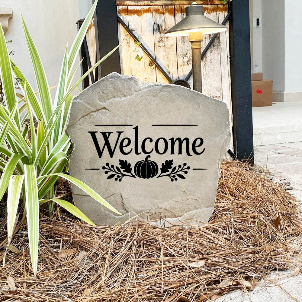 Fall Welcome Stone on pine straw next to a rustic garden gate and landscape light, engraved with a pumpkin motif