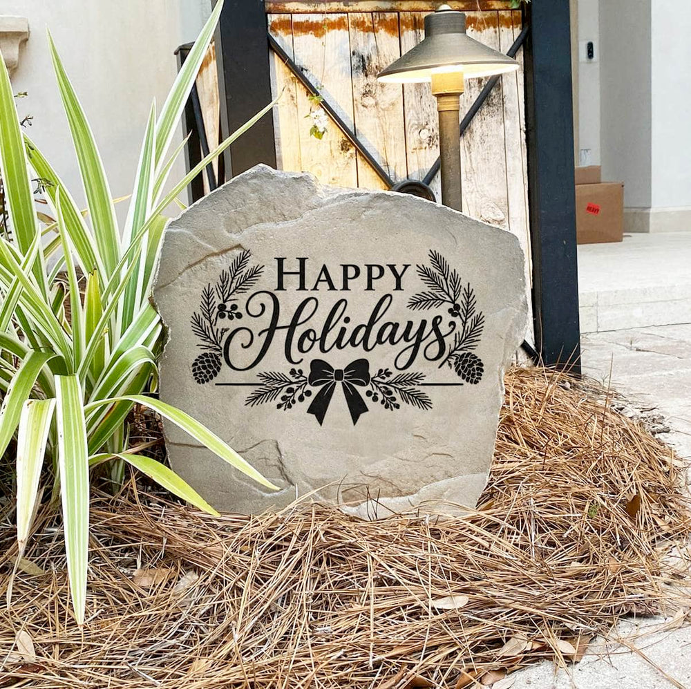 Happy Holidays Stone on pine straw next to a rustic garden gate and landscape light