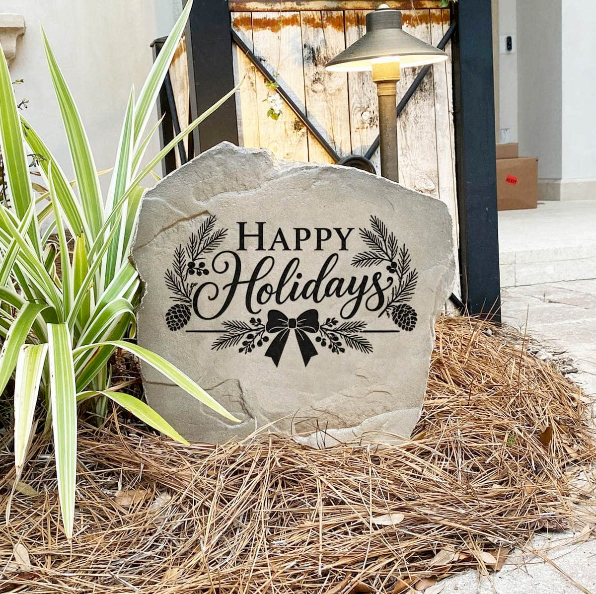 Happy Holidays Stone on pine straw next to a rustic garden gate and landscape light