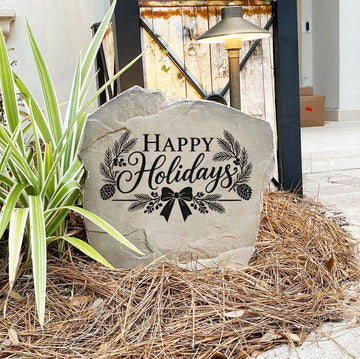 Happy Holidays Stone on pine straw next to a rustic garden gate and landscape light