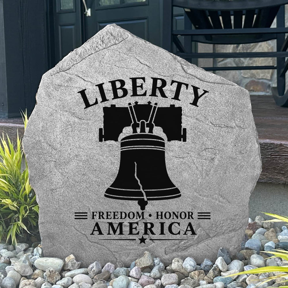 Decorative stone with 'Liberty Freedom Honor America' text and bell design on a pebble-covered ground.