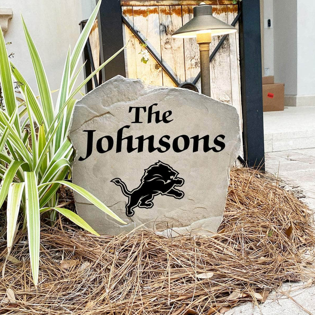 Custom Detroit Lions Name Stone displayed in a landscaped flower bed, showcasing personalized family lettering and officially licensed team artwork. This decorative outdoor stone creates a striking focal point for Lions fans and outdoor living spaces.