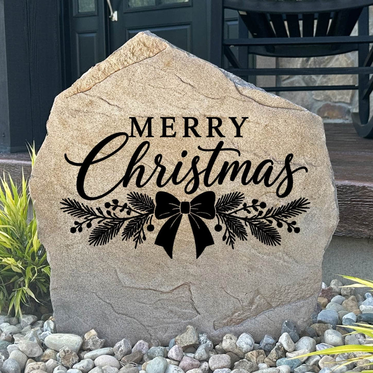 Sandstone Merry Christmas Stone engraved with script lettering, pine sprigs and a bow, set in river rock