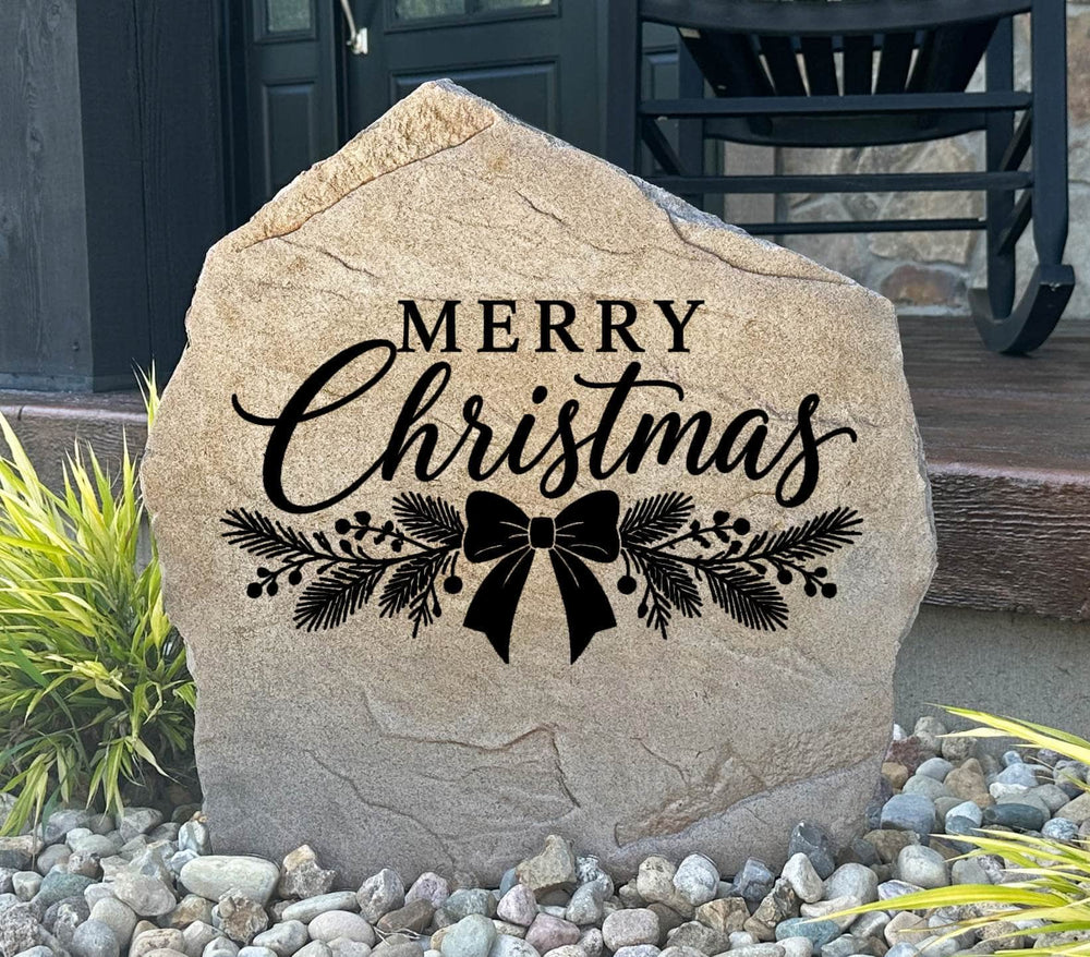 Sandstone Merry Christmas Stone engraved with script lettering, pine sprigs and a ribbon bow by a porch