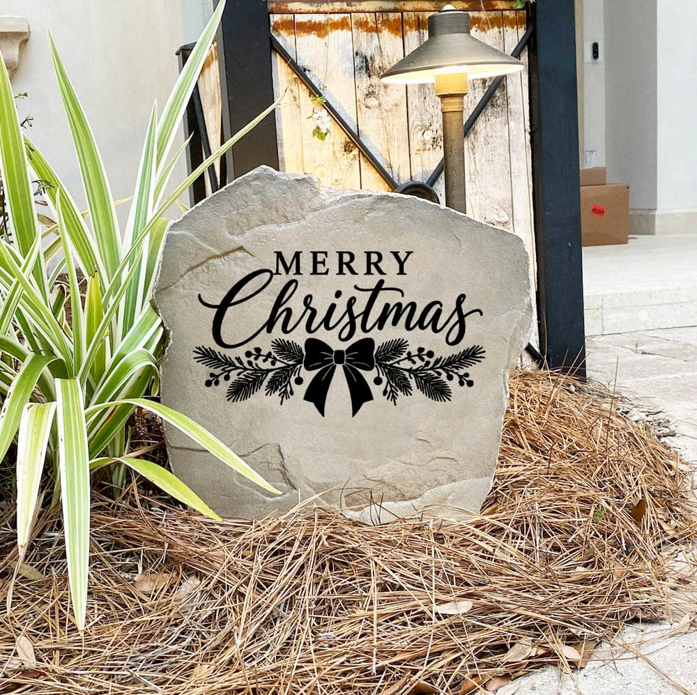 Merry Christmas Stone on pine straw next to a rustic garden gate and landscape light