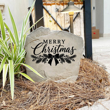 Merry Christmas Stone on pine straw next to a rustic garden gate and landscape light