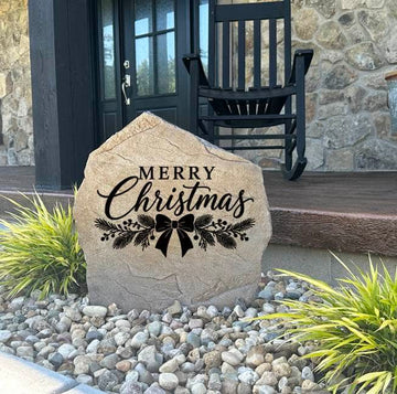Sandstone Merry Christmas Stone in a rock bed at a stone-front porch with a black rocking chair