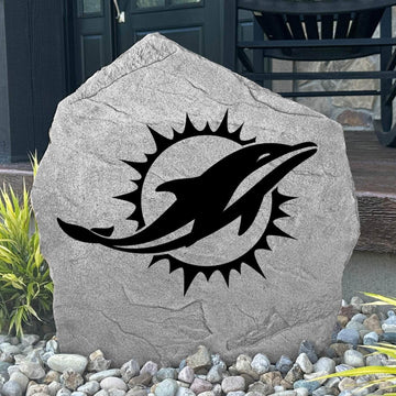 Custom Miami Dolphins Logo Stone displayed in a landscaped flower bed, showcasing officially licensed team artwork permanently engraved into the stone. This outdoor accent creates a bold focal point for Dolphins fans and outdoor living spaces.