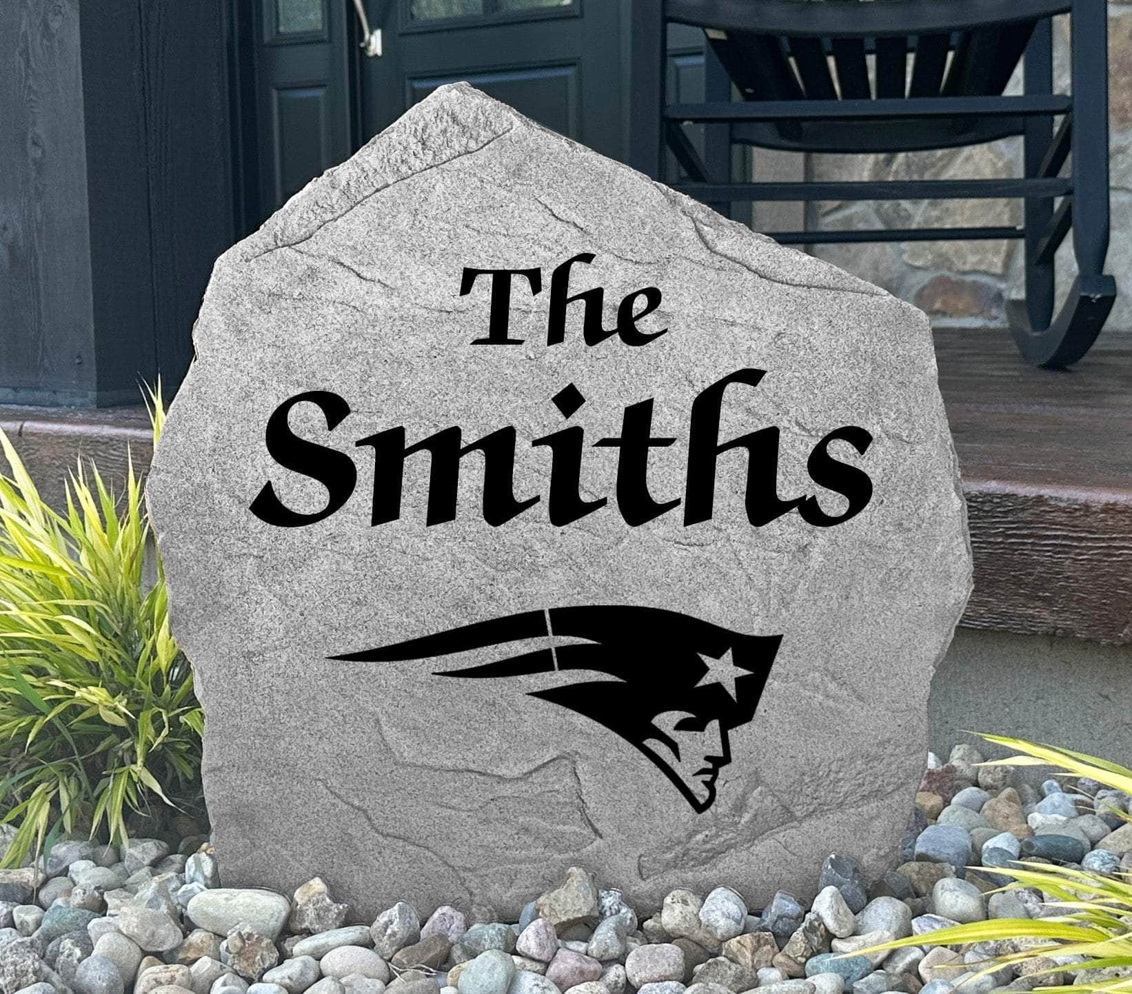 Custom New England Patriots Name Stone displayed in a landscaped flower bed, showcasing personalized family lettering and officially licensed team artwork. This decorative outdoor stone creates a striking focal point for Patriots fans and outdoor living spaces.