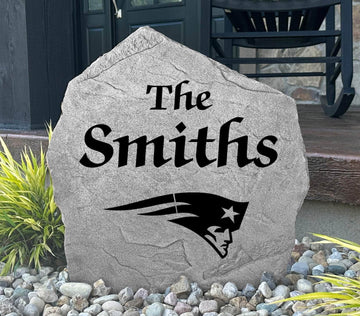 Custom New England Patriots Name Stone displayed in a landscaped flower bed, showcasing personalized family lettering and officially licensed team artwork. This decorative outdoor stone creates a striking focal point for Patriots fans and outdoor living spaces.