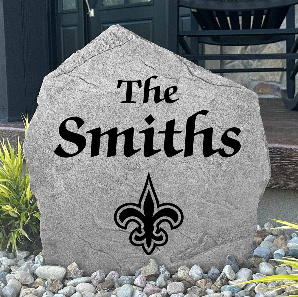 Custom New Orleans Saints Name Stone displayed in a landscaped flower bed, showcasing personalized family lettering and officially licensed team artwork. This decorative outdoor stone creates a striking focal point for Saints fans and outdoor living spaces.