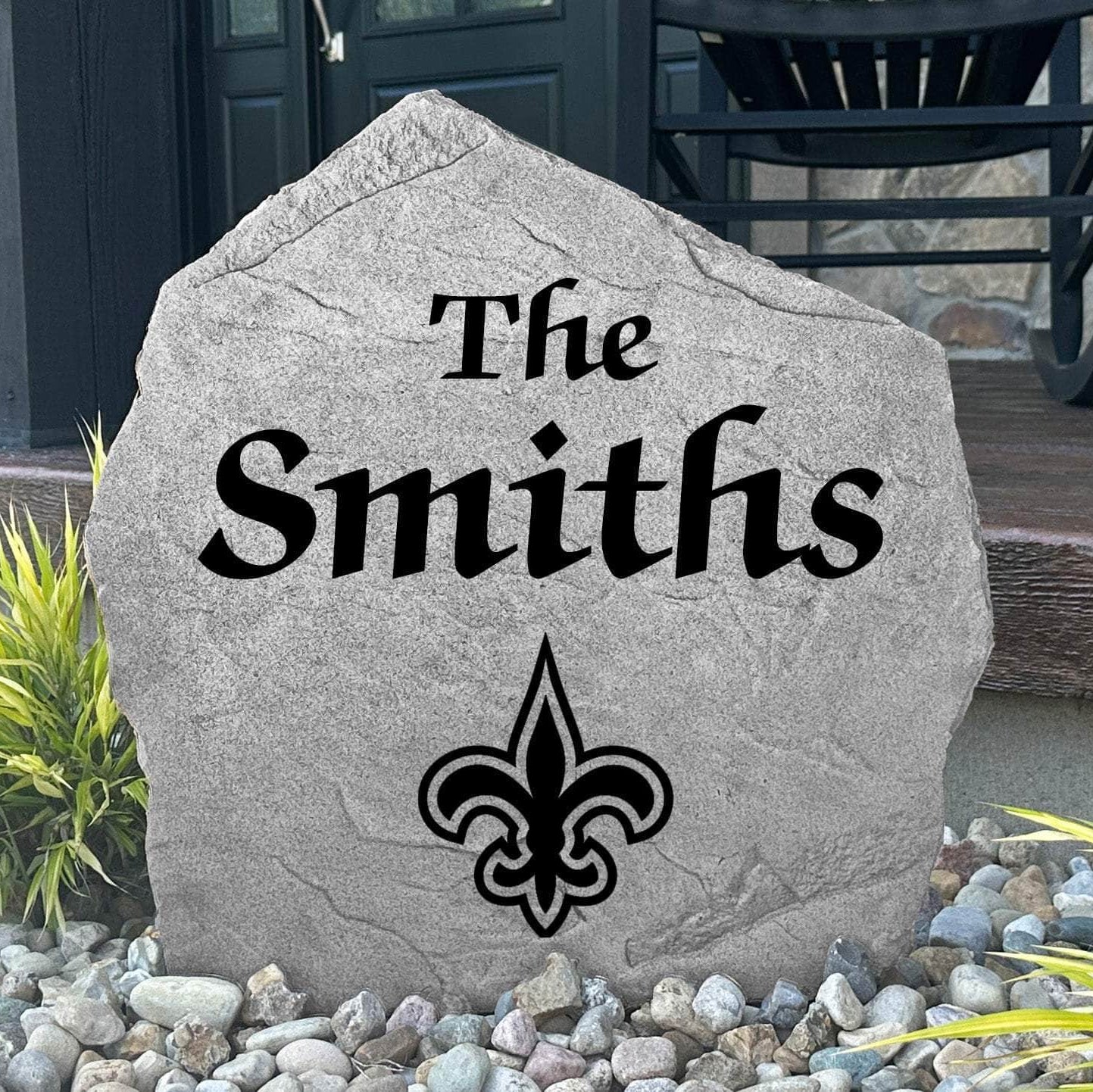 Custom New Orleans Saints Name Stone displayed in a landscaped flower bed, showcasing personalized family lettering and officially licensed team artwork. This decorative outdoor stone creates a striking focal point for Saints fans and outdoor living spaces.