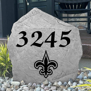 Custom New Orleans Saints Address Stone displayed in a landscaped flower bed with personalized house numbers and officially licensed team artwork. This engraved address marker creates a striking focal point for Saints fans and outdoor living spaces.