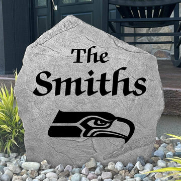 Custom Seattle Seahawks Name Stone displayed in a landscaped flower bed, showcasing personalized family lettering and officially licensed team artwork. This decorative outdoor stone creates a striking focal point for Seahawks fans and outdoor living spaces.