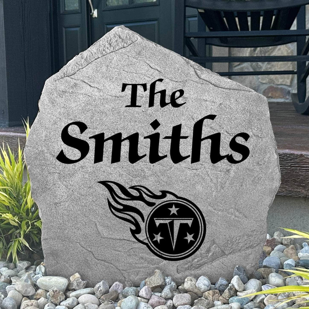 Custom Tennessee Titans Name Stone displayed in a landscaped flower bed, showcasing personalized family lettering and officially licensed team artwork. This decorative outdoor stone creates a striking focal point for Titans fans and outdoor living spaces.