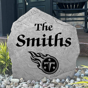 Custom Tennessee Titans Name Stone displayed in a landscaped flower bed, showcasing personalized family lettering and officially licensed team artwork. This decorative outdoor stone creates a striking focal point for Titans fans and outdoor living spaces.