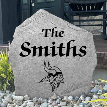 Custom Minnesota Vikings Name Stone displayed in a landscaped flower bed, showcasing personalized family lettering and officially licensed team artwork. This decorative outdoor stone creates a striking focal point for Vikings fans and outdoor living spaces.