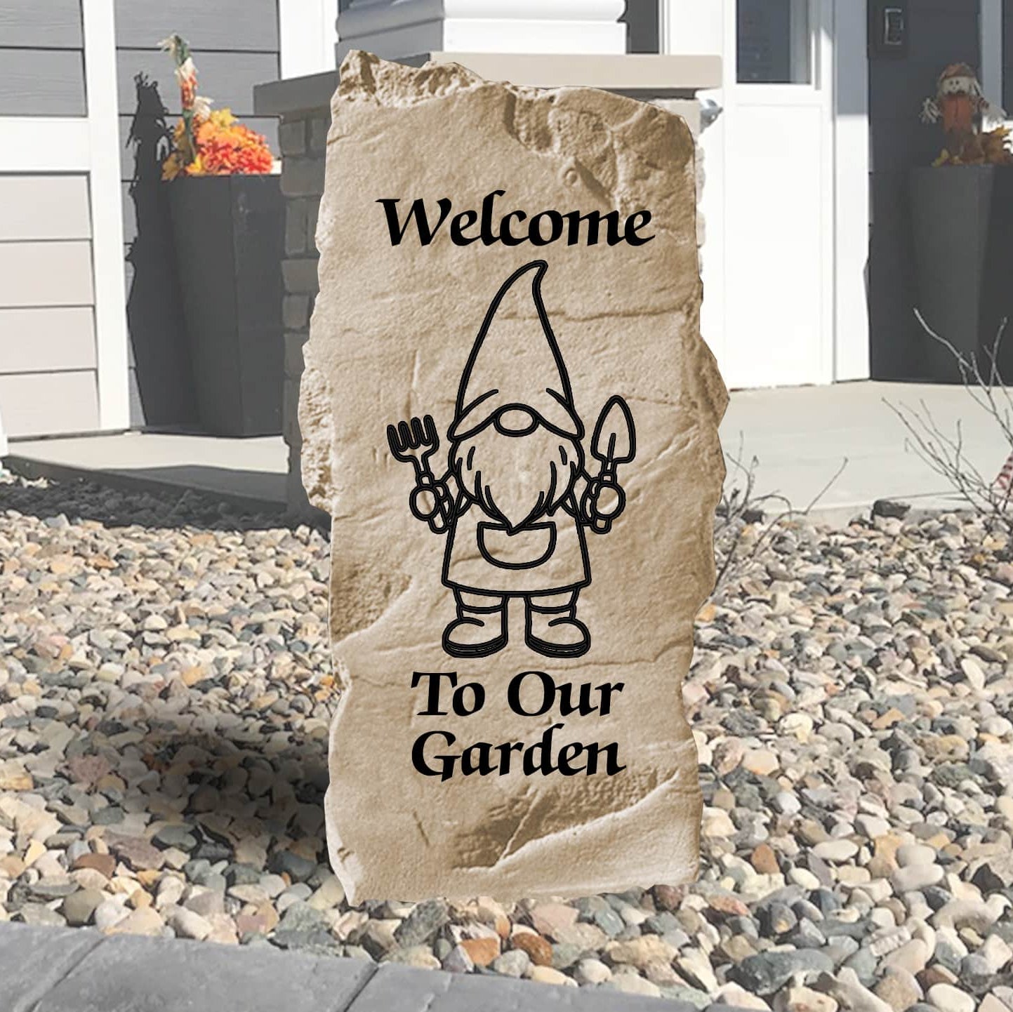 Decorative stone with a garden gnome illustration and 'Welcome To Our Garden' text on a pebbly ground.