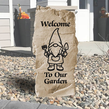 Decorative stone with a garden gnome illustration and 'Welcome To Our Garden' text on a pebbly ground.