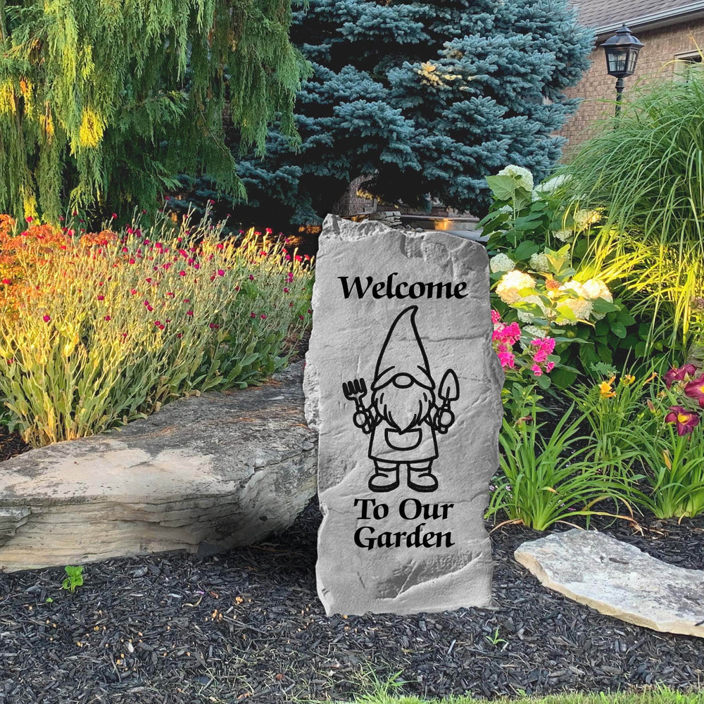 Decorative stone with a gnome illustration and 'Welcome To Our Garden' text in a garden setting.