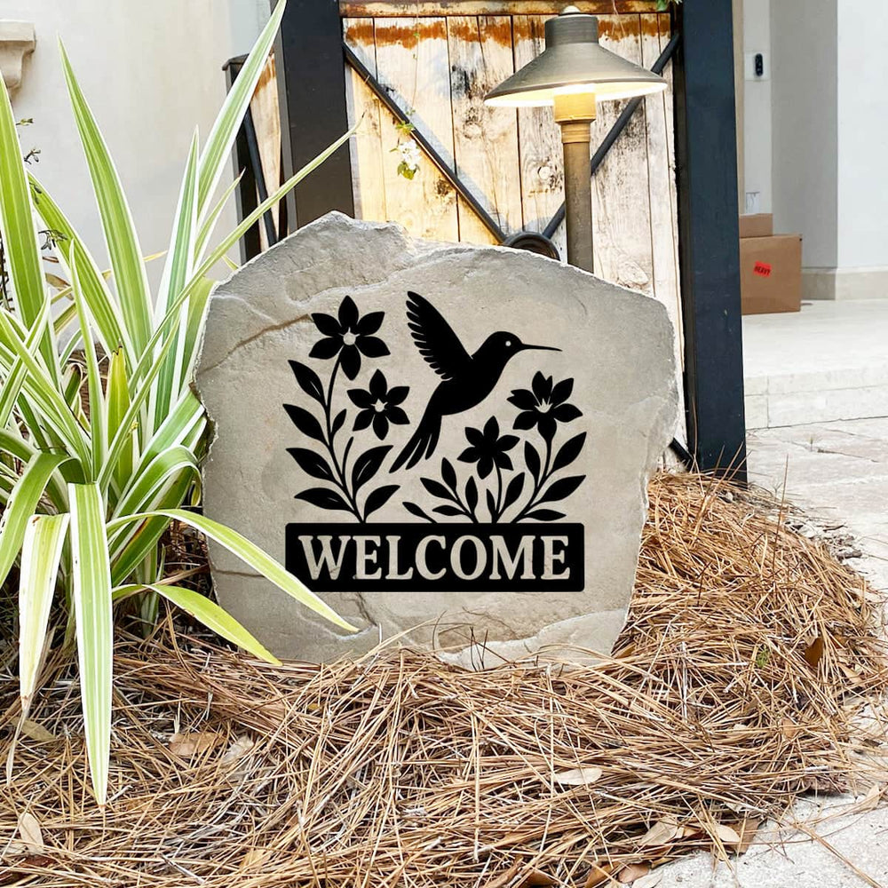 Engraved Welcome Hummingbird Stone nestled among colorful flowers and greenery, bringing nature-inspired beauty to the landscape. This weather-resistant garden accent provides lasting elegance and inviting curb appeal.
