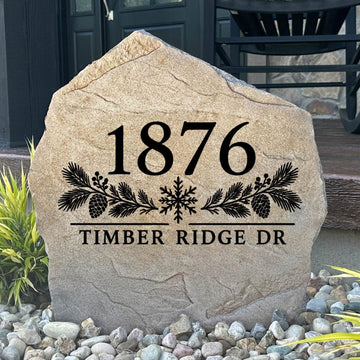 Winter Address Stone engraved 1876 Timber Ridge Dr with pine boughs and a snowflake, set in river rock by a porch
