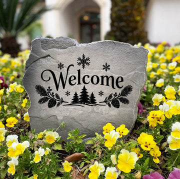 Gray Winter Welcome Stone with snowflakes and evergreens standing in a bed of yellow and purple pansies