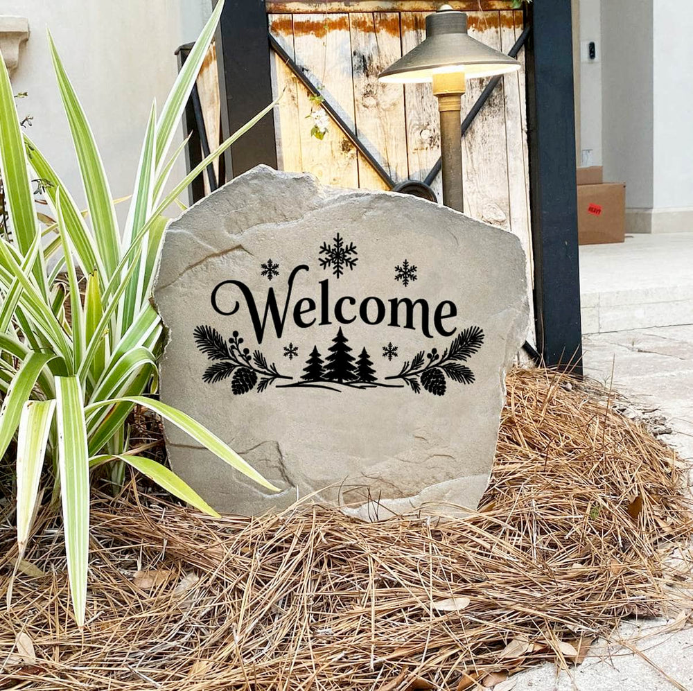Winter Welcome Stone on pine straw next to a rustic garden gate and landscape light, engraved with pine trees