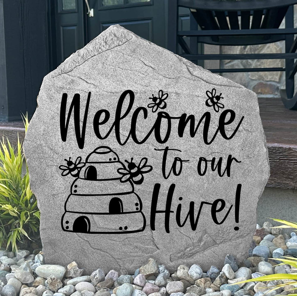 Custom Welcome Hive Stone displayed in a landscaped garden, showcasing detailed bee-themed artwork engraved directly into the stone surface. Perfect for pollinator gardens, walkways, and backyard landscapes.