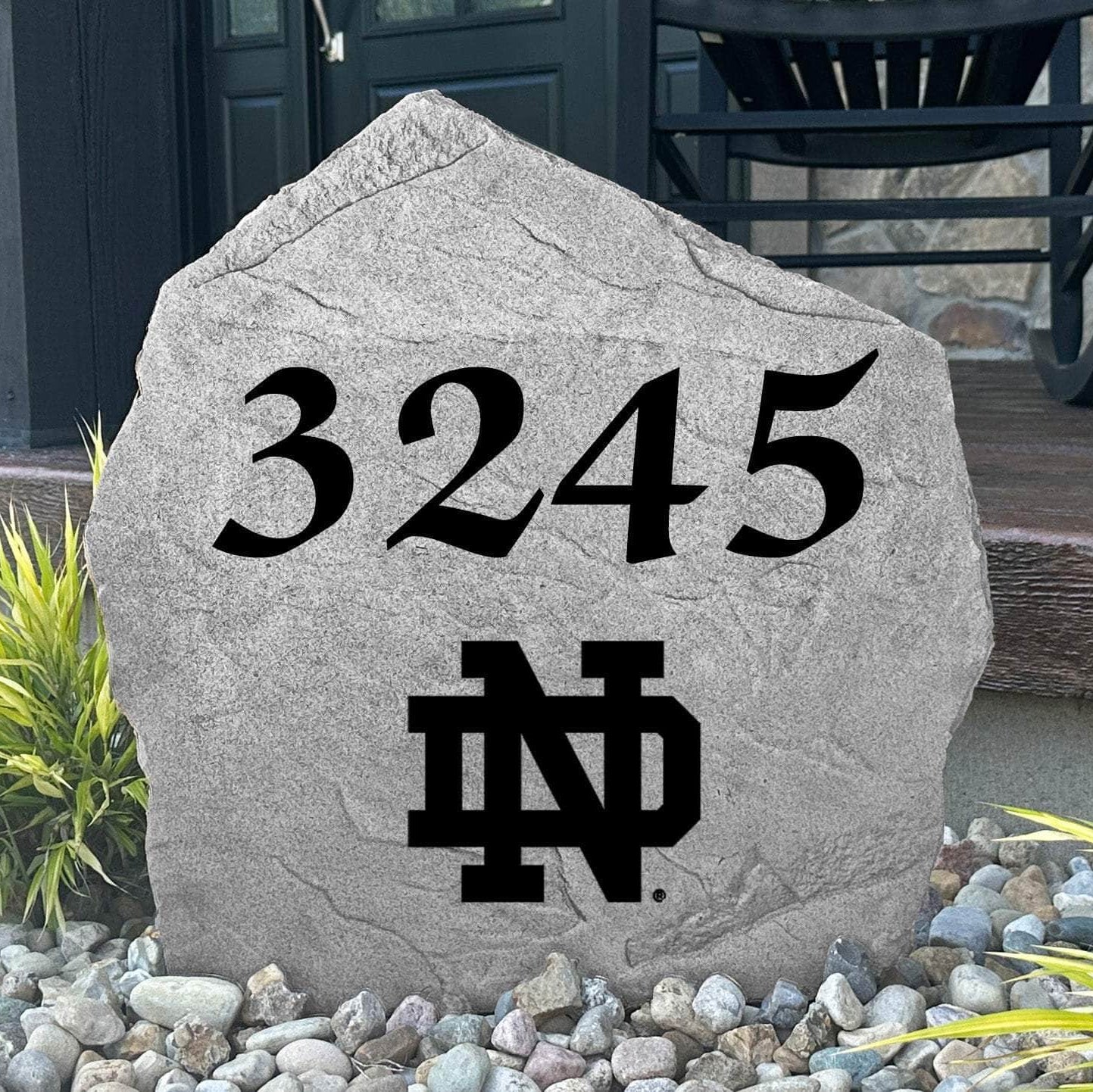 Custom University of Notre Dame Address Stone displayed in a landscaped flower bed, showcasing personalized house numbers and officially licensed Fighting Irish artwork. This engraved address stone creates a beautiful focal point for alumni homes and outdoor spaces.