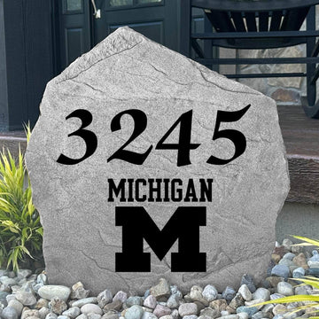 Custom University of Michigan Address Stone displayed in a landscaped flower bed, showcasing personalized house numbers and officially licensed Wolverines artwork. This engraved address stone creates a beautiful focal point for alumni homes and outdoor spaces.
