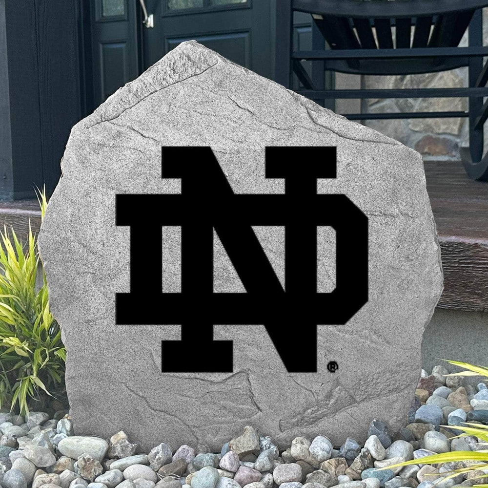 Custom University of Notre Dame Logo Stone displayed in a landscaped flower bed, showcasing officially licensed Fighting Irish artwork with permanent engraving. This decorative outdoor stone creates a beautiful focal point for alumni homes and Notre Dame fans.