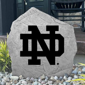 Custom University of Notre Dame Logo Stone displayed in a landscaped flower bed, showcasing officially licensed Fighting Irish artwork with permanent engraving. This decorative outdoor stone creates a beautiful focal point for alumni homes and Notre Dame fans.