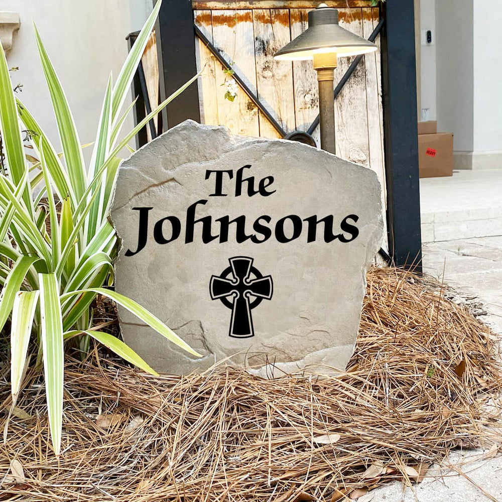 Engraved Celtic Cross Name Stone nestled among colorful flowers and greenery, combining custom family personalization with classic Celtic artwork. This weather-resistant garden stone provides lasting beauty and curb appeal.