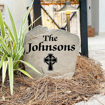 Engraved Celtic Cross Name Stone nestled among colorful flowers and greenery, combining custom family personalization with classic Celtic artwork. This weather-resistant garden stone provides lasting beauty and curb appeal.