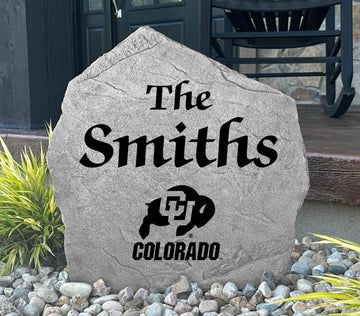 Custom University of Colorado Name Stone displayed in a landscaped flower bed, showcasing personalized family lettering and officially licensed Colorado Buffaloes artwork. This decorative outdoor stone creates a beautiful focal point for alumni homes and Buffaloes fans.
