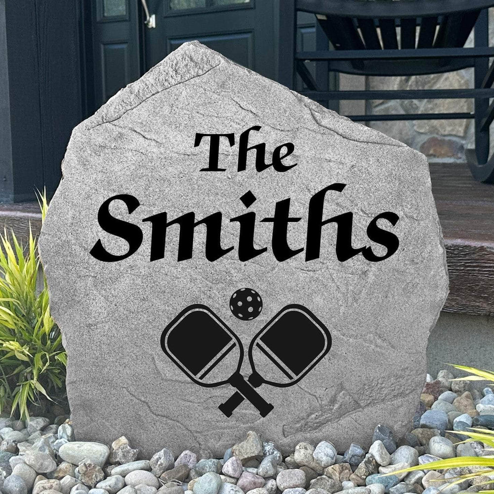 Custom Pickleball Name Stone displayed in a landscaped flower bed, showcasing personalized names and detailed pickleball-themed engraving. This unique garden stone creates a fun focal point for entryways and outdoor living spaces.