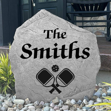 Custom Pickleball Name Stone displayed in a landscaped flower bed, showcasing personalized names and detailed pickleball-themed engraving. This unique garden stone creates a fun focal point for entryways and outdoor living spaces.