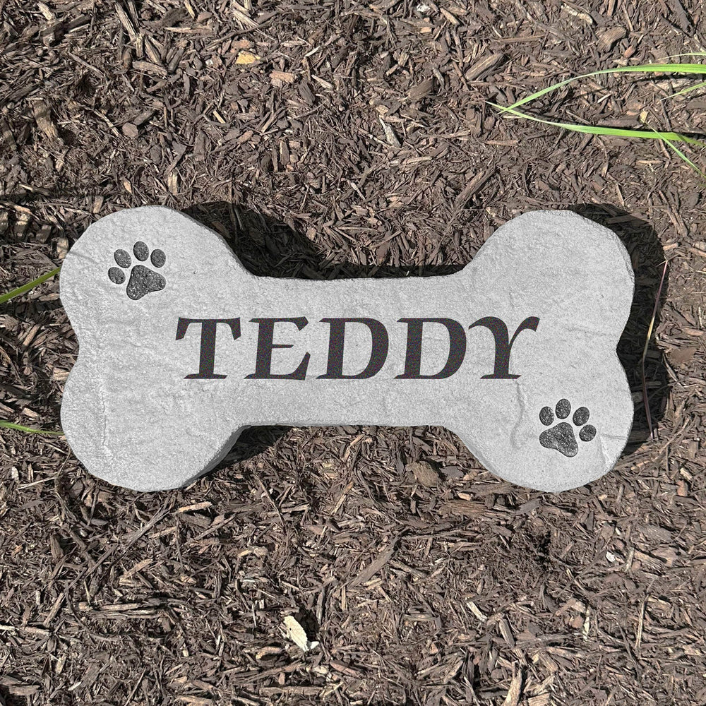 Custom Dog Bone Stone displayed in a landscaped flower bed, showcasing pet-inspired design and detailed engraving carved directly into the stone surface. Perfect for dog owners and outdoor pet spaces.