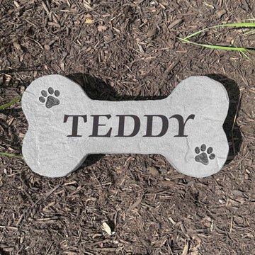 Custom Dog Bone Stone displayed in a landscaped flower bed, showcasing pet-inspired design and detailed engraving carved directly into the stone surface. Perfect for dog owners and outdoor pet spaces.