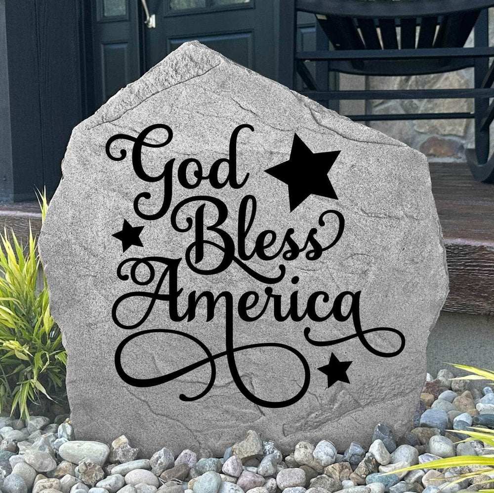 God Bless America Stone displayed in a beautifully landscaped flower bed, showcasing patriotic artwork and a meaningful message. This weather-resistant outdoor stone creates a striking focal point for gardens and walkways.