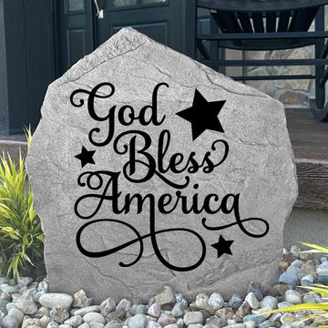 God Bless America Stone displayed in a beautifully landscaped flower bed, showcasing patriotic artwork and a meaningful message. This weather-resistant outdoor stone creates a striking focal point for gardens and walkways.