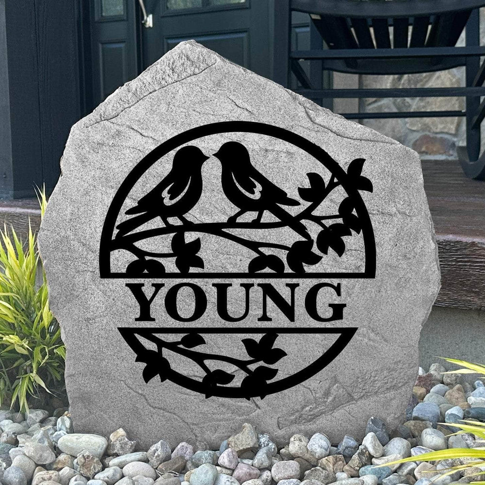 Custom Love Birds Monogram Stone displayed in a landscaped flower bed, showcasing romantic bird artwork and personalized engraving. This engraved outdoor stone creates a beautiful focal point for walkways and home entrances.