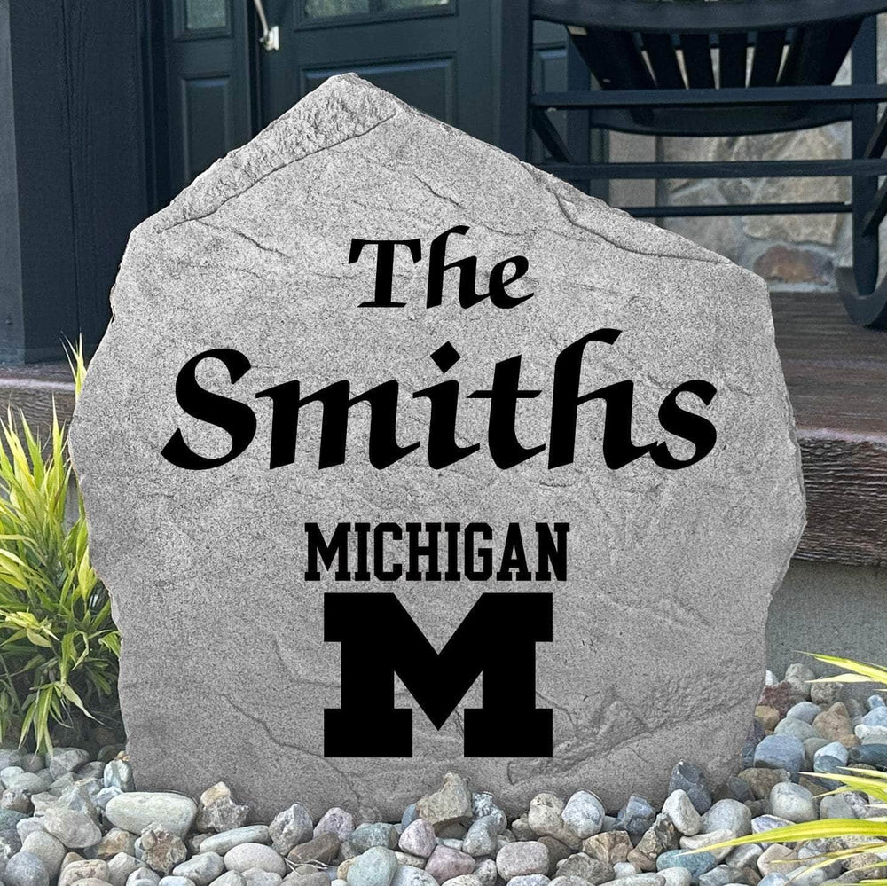 Custom University of Michigan Name Stone displayed in a landscaped flower bed, showcasing personalized family lettering and officially licensed Wolverines artwork. This engraved outdoor stone creates a beautiful focal point for alumni homes and Michigan fans.