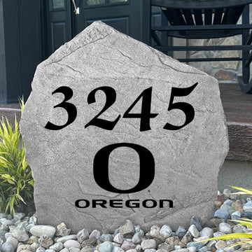 Custom University of Oregon Address Stone displayed in a landscaped flower bed, showcasing personalized house numbers and officially licensed Oregon Ducks artwork. This engraved address stone creates a beautiful focal point for alumni homes and outdoor spaces.